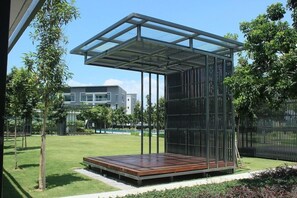 Un área de estar moderna al aire libre con techo de cristal, rodeada de follaje y una piscina.