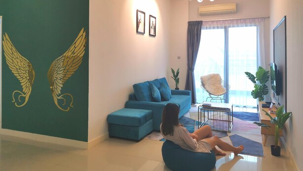 A modern living room with a blue sofa, a child sitting on a bean bag, and a large TV on the wall. - Sunset & Seaview Vacation Condo City Centre @ Imago Shopping Mall (Kota Kinabalu)