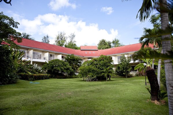 Un bâtiment doté d’un toit rouge, entouré d’une pelouse bien entretenue et de diverses plantes tropicales.