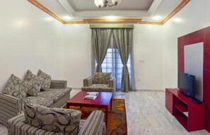 Una sala de estar con un conjunto de sofás, una mesa de centro, un televisor sobre un mueble bajo y una ventana con cortinas.