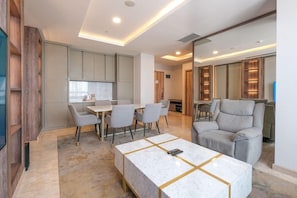 A modern living room with a marble coffee table, grey sofas, and a dining area with chairs. - Bigland Hotel Bogor (Bogor)