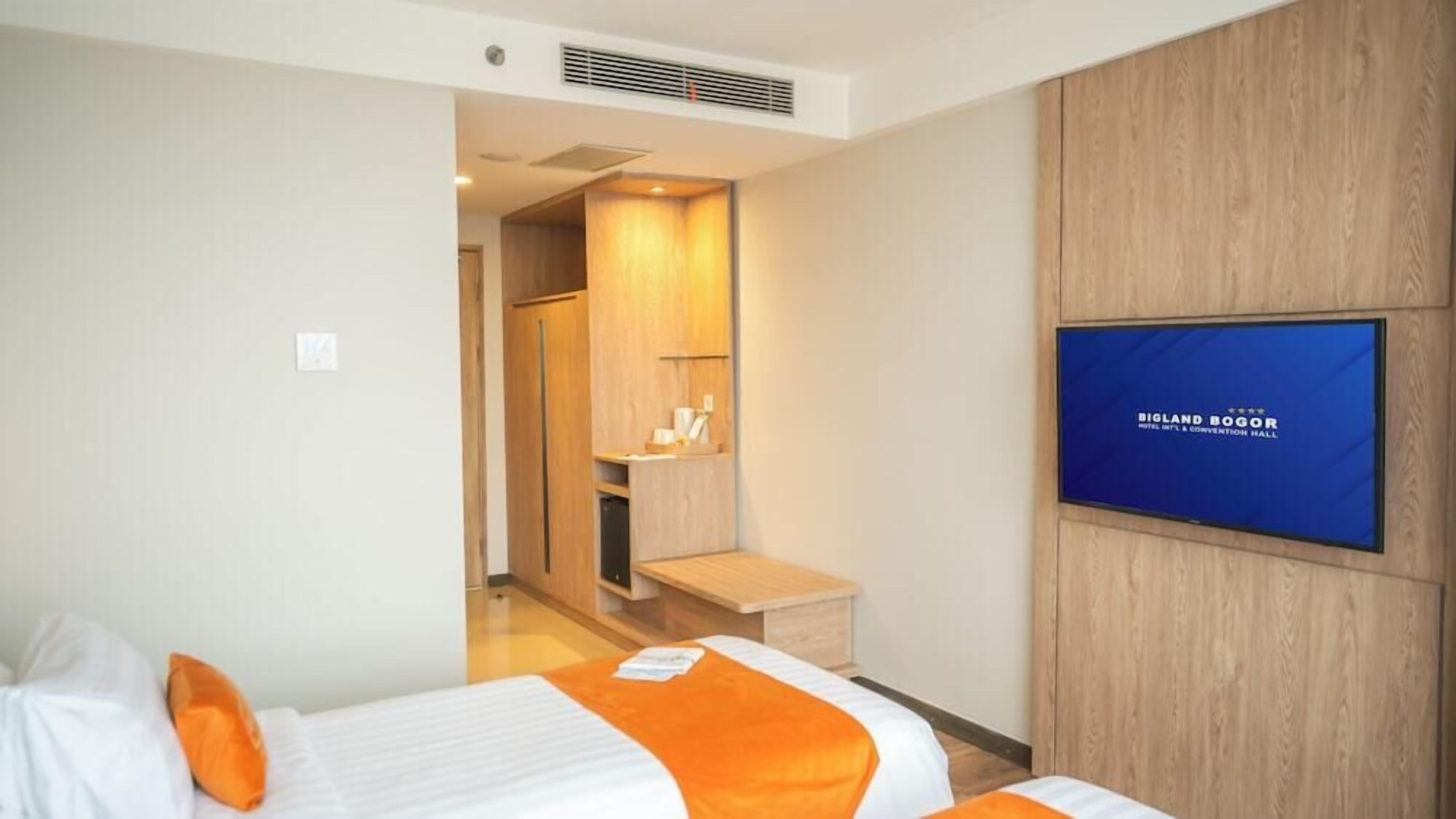 A hotel room with two beds, a TV, a wooden wardrobe, and a small table.
