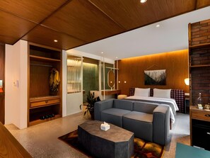 Une chambre d’hôtel moderne avec un plafond en bois, un grand lit, un canapé gris, une petite table basse et une armoire.
