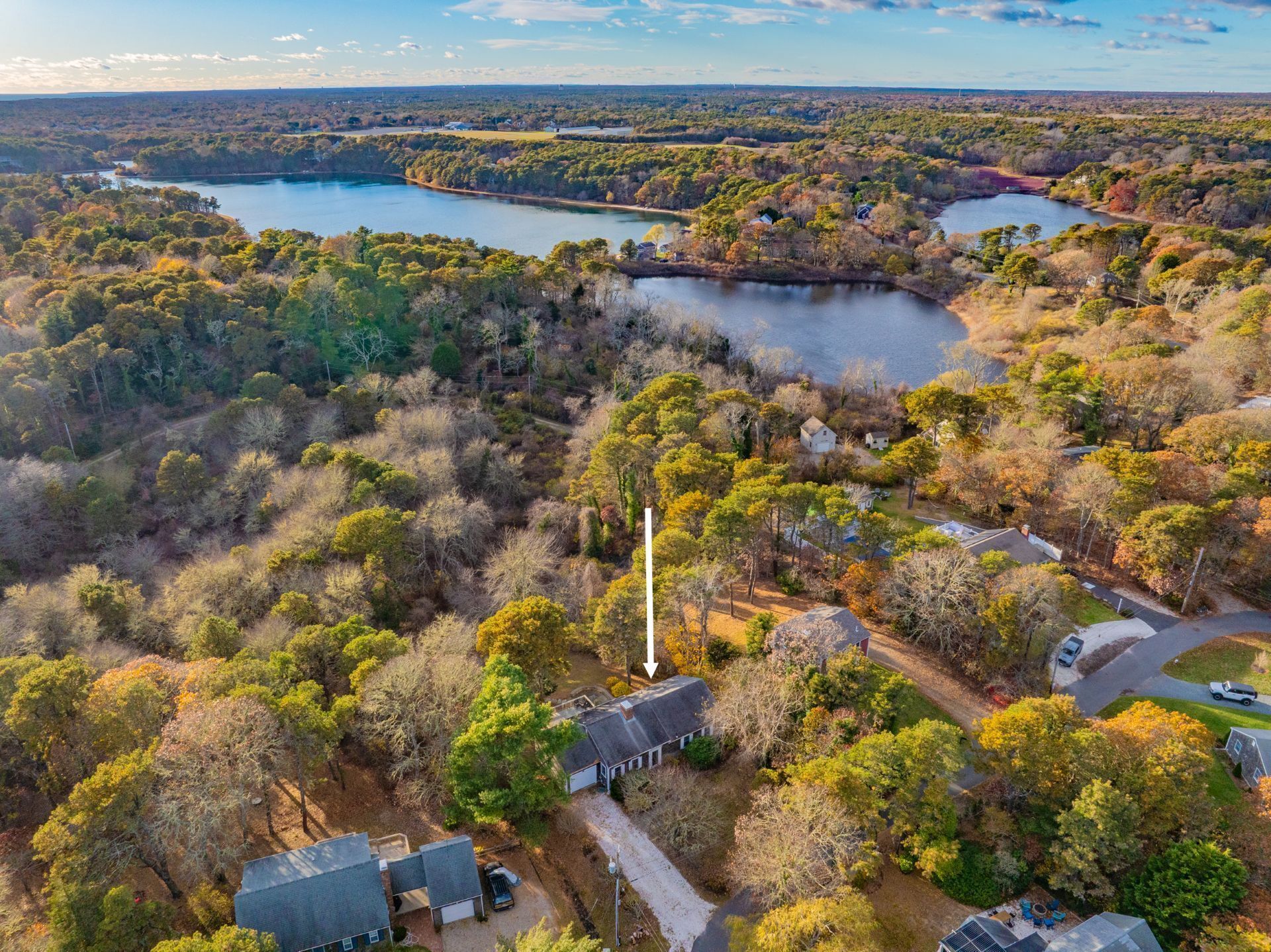 An aerial view of a residential area with houses, a lake, and surrounding forest.