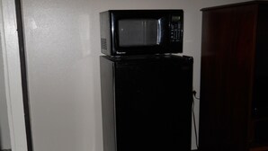 A black refrigerator with a microwave on top, located in a corner with a wooden cabinet nearby.