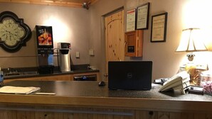 A hotel reception area with a wooden counter, a clock, a fruit juice dispenser, a coffee machine, a laptop, and a lamp. - THE RED Lodge INN (Red Lodge)