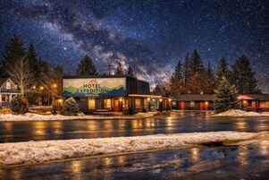 A hotel named 'Hotel Expedition Montana' with a starry night sky, snow-covered ground, and a parking lot.