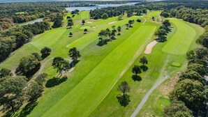 Vista aérea de un campo de golf con varios fairways, búnkeres de arena y un cuerpo de agua al fondo.
