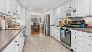 Una cocina moderna con armarios blancos, electrodomésticos de acero inoxidable y una zona de comedor con sillas de madera.