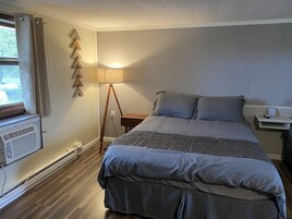 Un dormitorio con cama, mesita de noche, lámpara, calentador y ventana con cortinas.