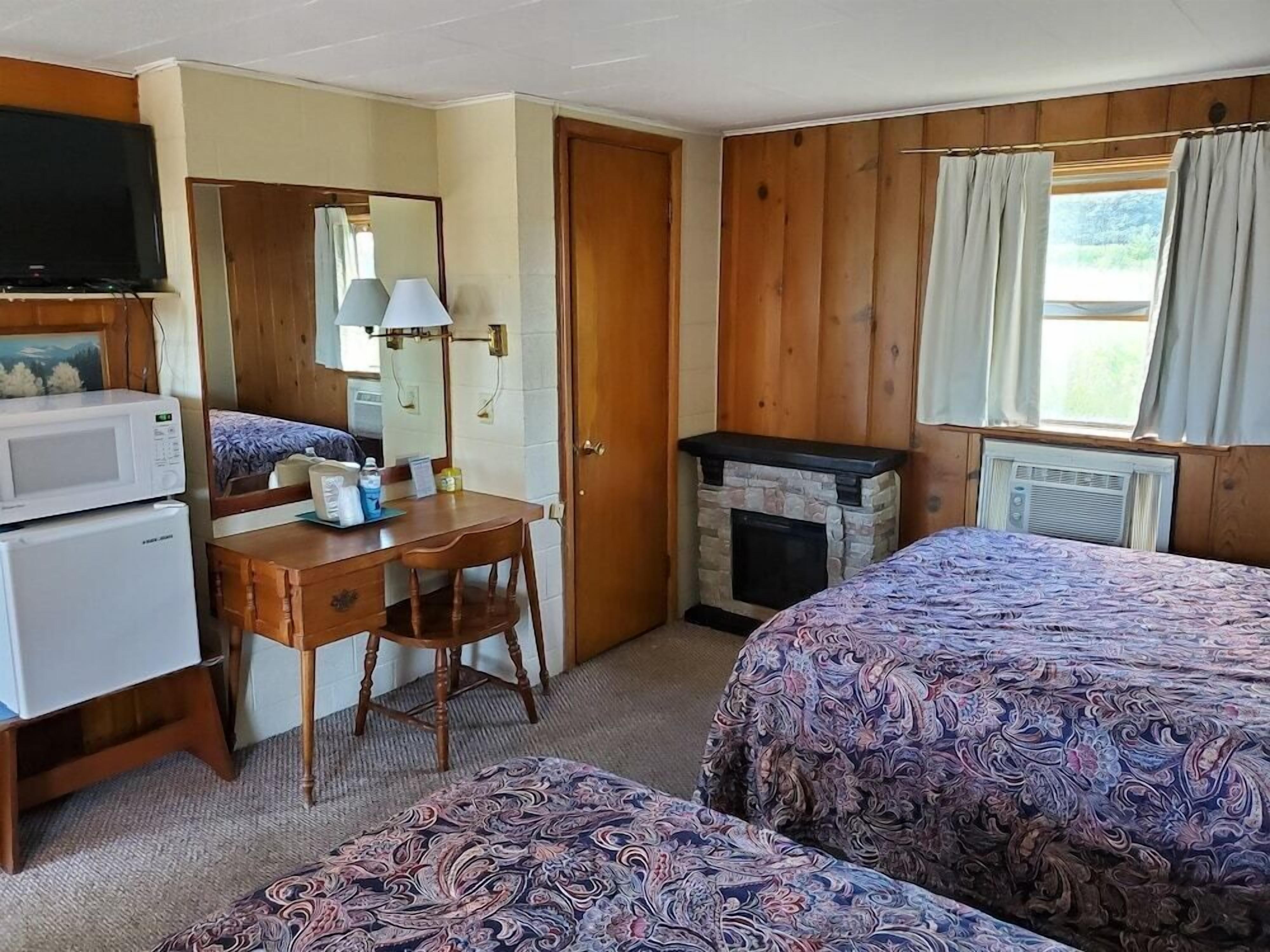 A room with a bed, a desk with a chair, a television, a microwave, a fireplace, and a window with curtains.