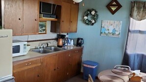 A compact kitchen with wooden cabinets, a microwave, a sink, and a ceiling fan. - Gateway Motel (Hart)