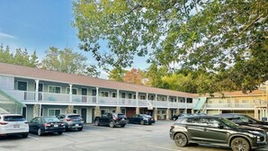 Un motel de dos pisos, un estacionamiento y una fila de coches estacionados al frente.