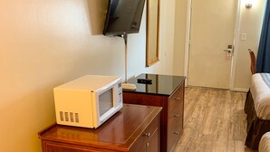 Habitación de hotel con microondas sobre una mesa de madera, televisor en la pared y cama con cortina azul.