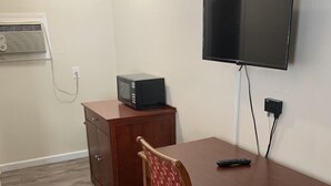 Una habitación pequeña con una mesa de madera, una silla, un televisor fijado a la pared y un microondas en un mueble.