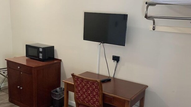 Una habitación pequeña con cama, escritorio, silla, televisión y microondas.