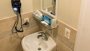 Un baño con lavamanos, secador de pelo y artículos de aseo en un estante.