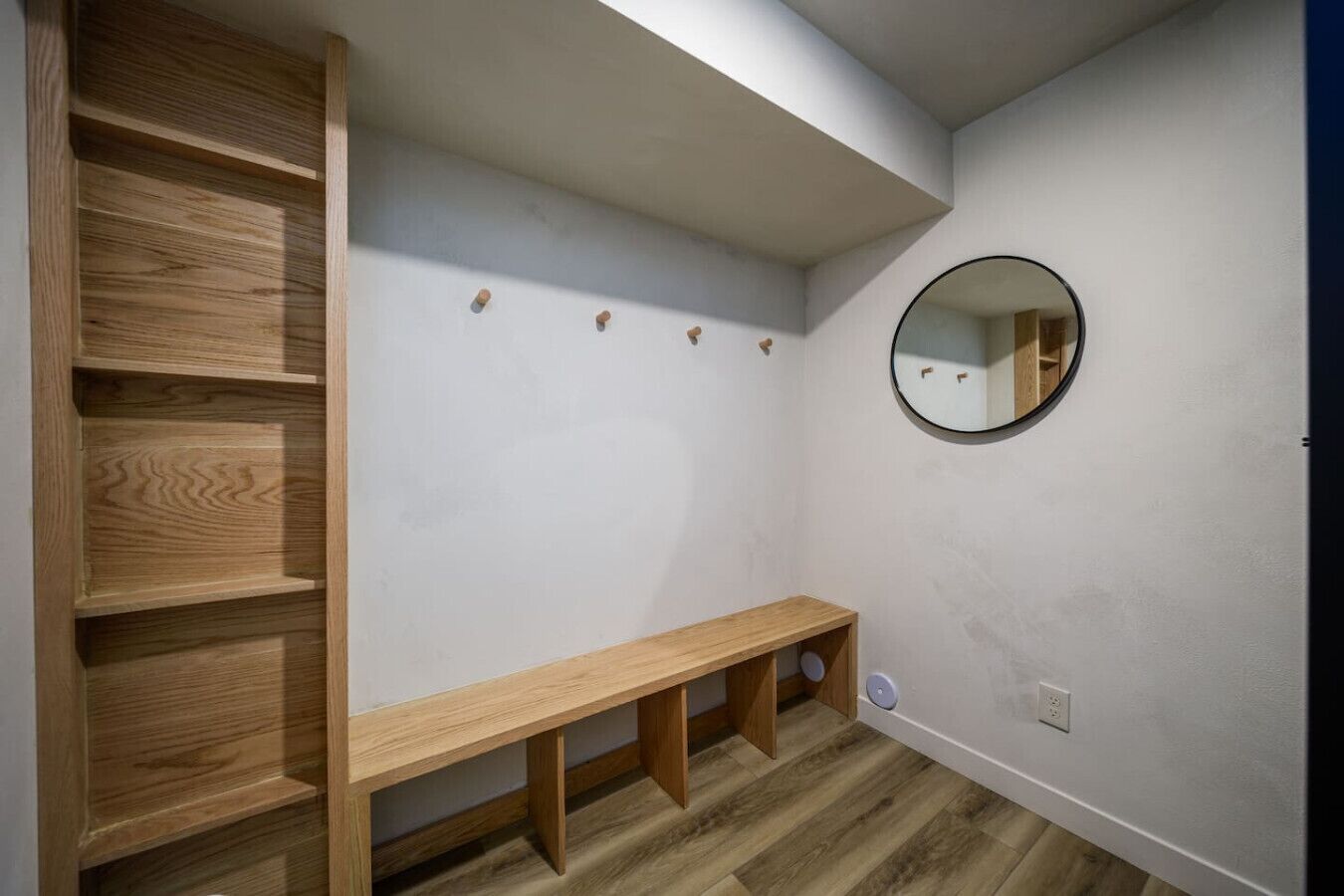 Ein Zimmer mit einer Holzbank, einem runden Spiegel an der Wand und einer eingebauten Holzregaleinheit.
