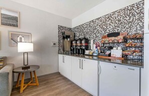A compact kitchenette with a coffee machine, a refrigerator, and a microwave. There is a small round table with a lamp beside the kitchenette. - Woodspring Suites Portland North Gresham (Portland)