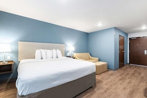 A hotel room with a large bed, a bedside table, a chair, and a wardrobe. - Woodspring Suites Portland North Gresham (Portland)
