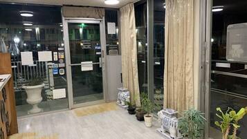 A hotel lobby with a wooden floor, potted plants, and a glass door leading outside.