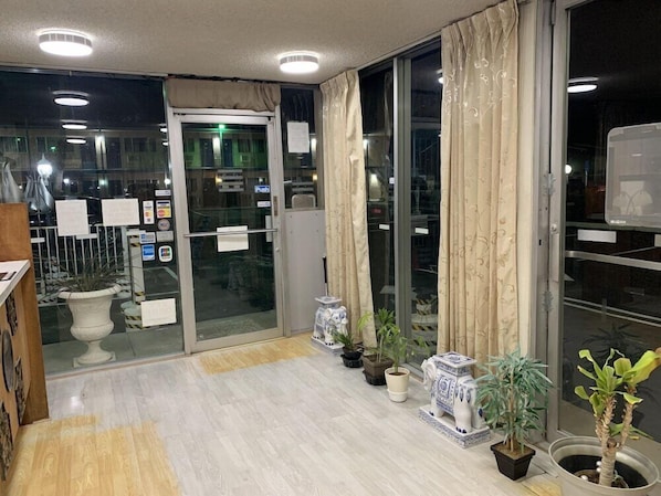 A hotel lobby with a wooden floor, potted plants, and a glass door leading outside. - Best Motel (Mojave)