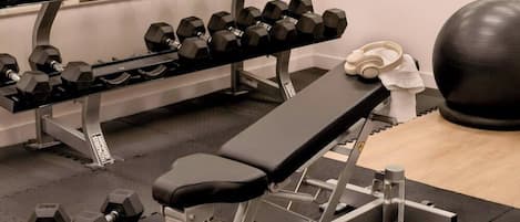 Une salle de sport équipée d’un banc de développé couché, d’haltères et d’un vélo d’appartement.