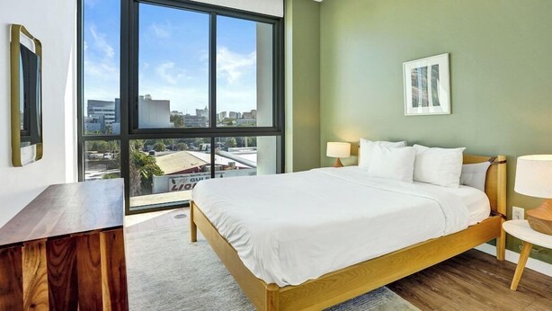 A modern hotel room with a large window, a wooden bed, a desk, and a view of the cityscape. - Sonder 17west (Miami Beach)