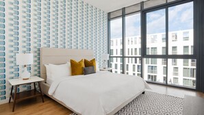 A modern hotel room with a large bed, a nightstand, a patterned rug, and a view of the city through large windows. - Sonder 17west (Miami Beach)