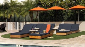 Un espace aménagé au bord de la piscine, avec des chaises longues et des parasols orange, le tout entouré de verdure.