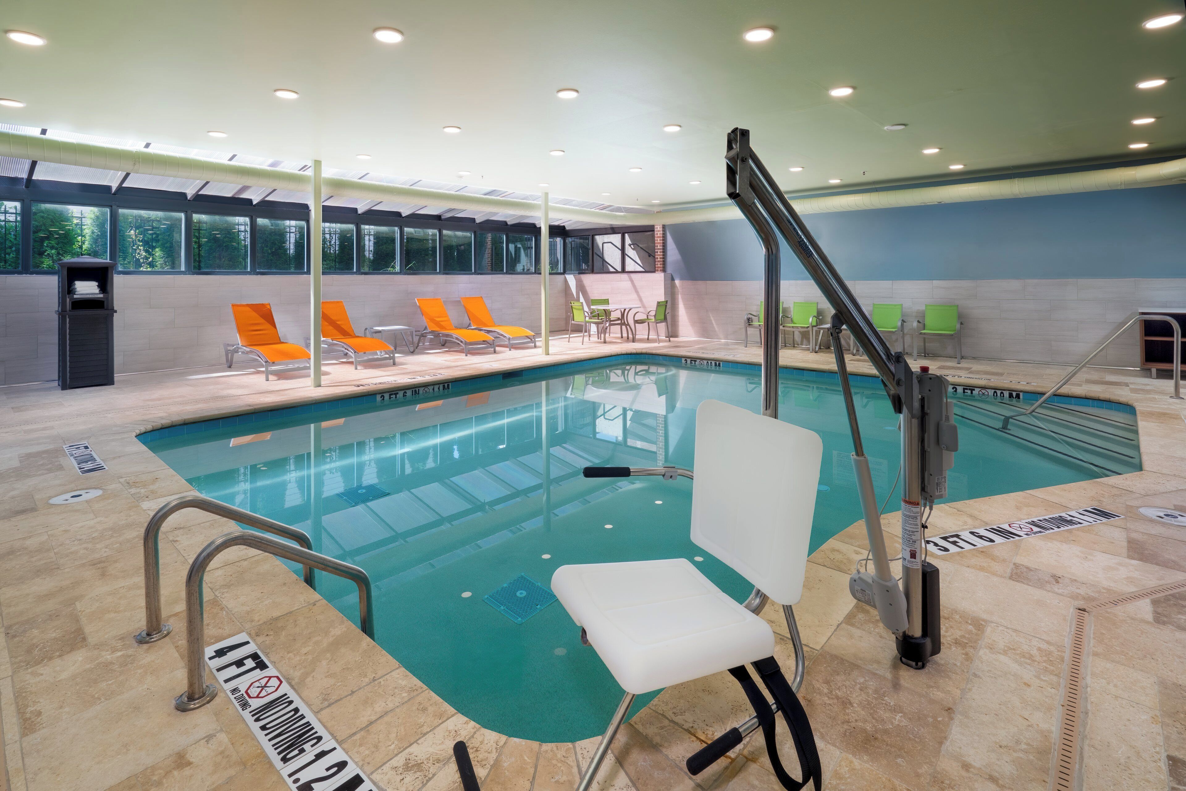 An indoor swimming pool with a clear water surface, surrounded by lounge chairs and a changing room.