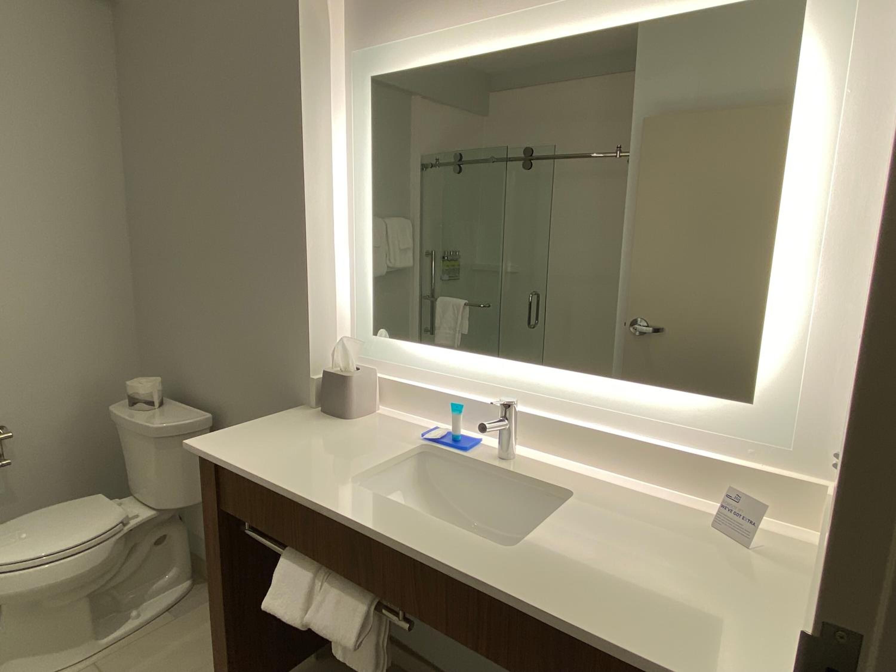 A modern bathroom with a large mirror, white sink, and a towel rack.