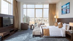 A hotel room with a large bed, a TV, a sofa, and a view of the city. - Seiba Serviced Apartment- Riyadh (Riyadh)