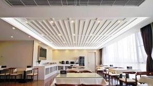 Comedor moderno de hotel con una isla central, varias mesas y sillas, y un techo con luminarias lineales.