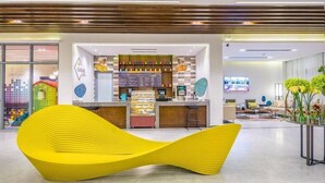 Una cafeteria moderna amb una zona de seients groga i original, una barra amb menú i una pantalla de televisió.