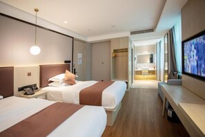 Habitación de hotel con dos camas, televisión, escritorio y un baño visible al fondo.