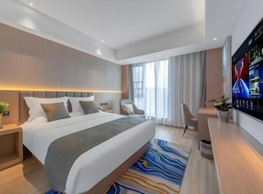 Habitación de hotel moderna con una cama grande, televisión de pantalla plana, escritorio y ventana con cortinas.