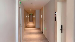 Un couloir d’hôtel avec des portes des deux côtés, un plancher en bois et un plafond doté d’un éclairage encastré.