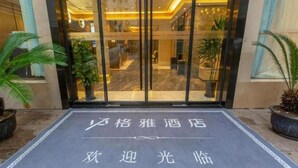 L’entrée d’un hôtel, avec une porte en verre, des plantes en pot de chaque côté et un paillasson orné de caractères chinois.