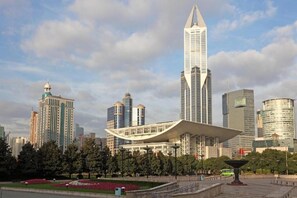 A cityscape with modern high-rise buildings, a distinctive white structure with a curved roof, and a park area with trees and flowers. - GYA Shanghai Long Distance Passenger Terminal Hotel (Shanghai)