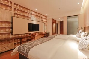 Una camera d'albergo moderna con un letto grande, una televisione a parete, una scrivania con sedie e una parete decorata con mensole.