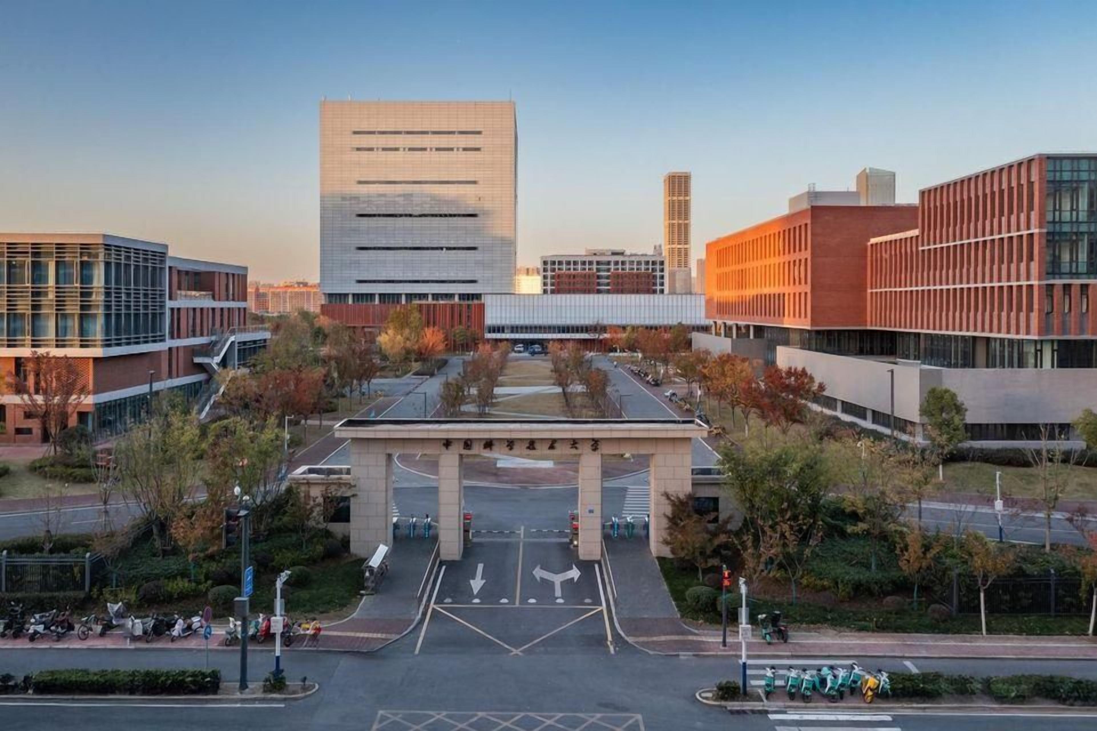 A modern building complex with a central entrance, multiple parking areas, and surrounding greenery.