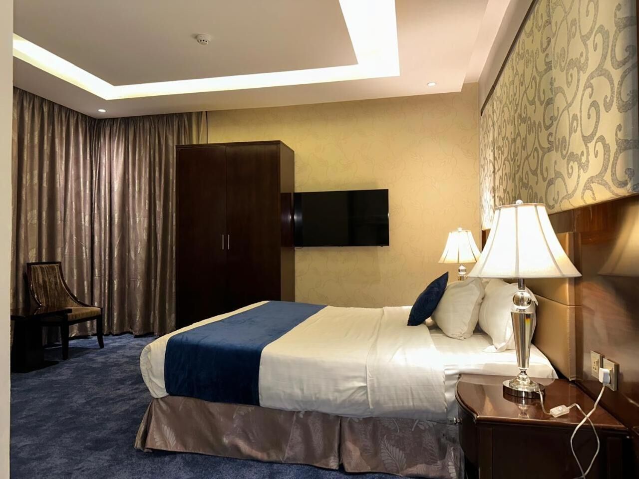 Een hotelkamer met een bed, nachtlampjes, een kledingkast, een bureau en een stoel.
