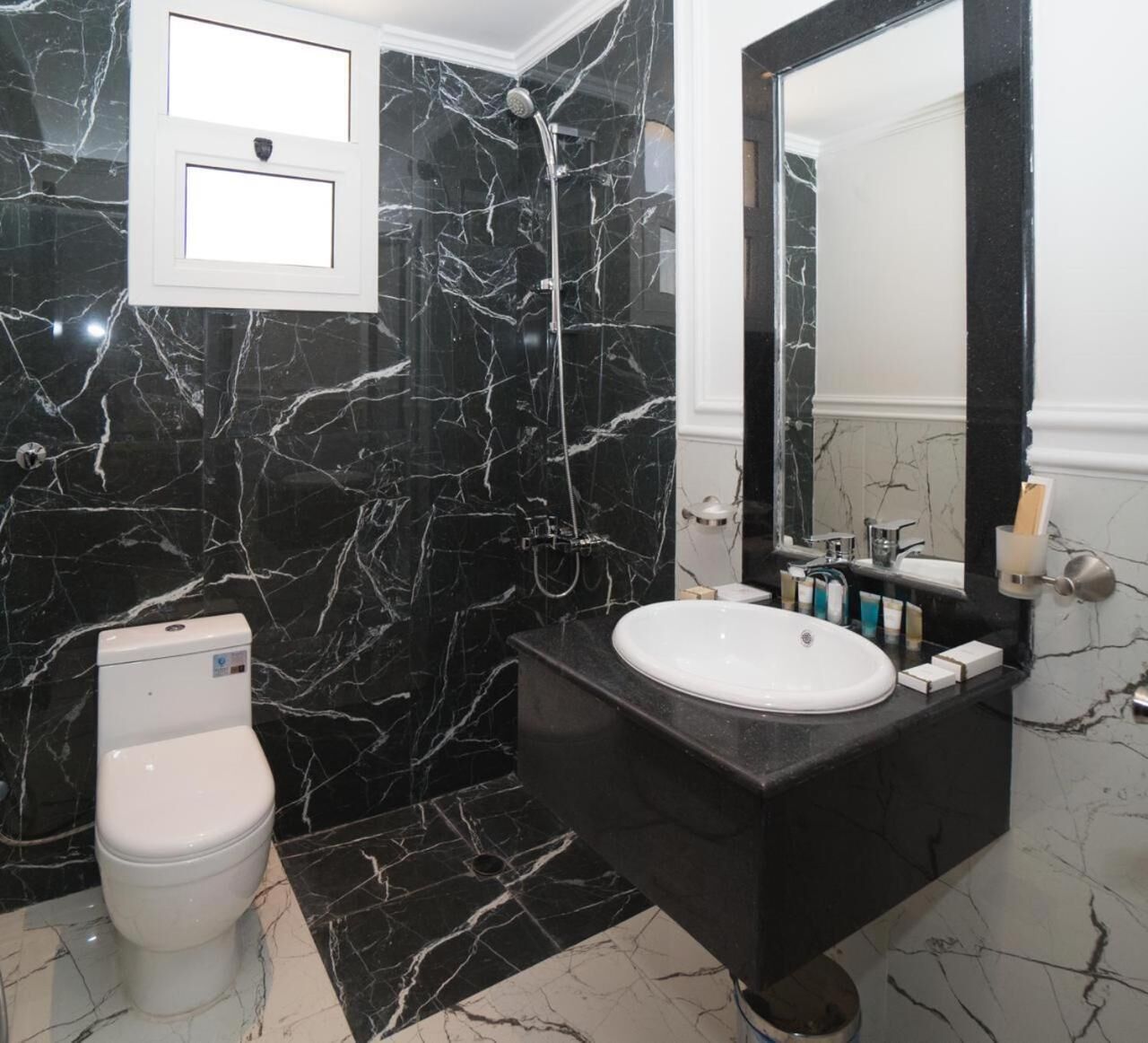 A bathroom with a black marble wall, a white toilet, a sink with a black countertop, and a large mirror.