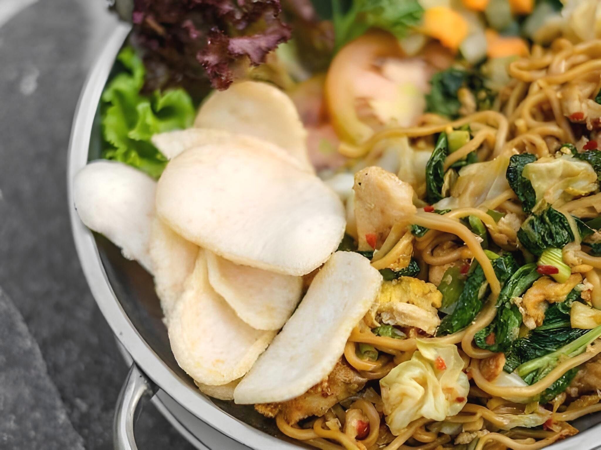 A bowl of noodles with vegetables and slices of white bread.