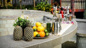 A stone counter with fresh pineapples, lemons, and limes, and various bottles and glasses. - La Luna Resort Yogyakarta (Ngaglik)