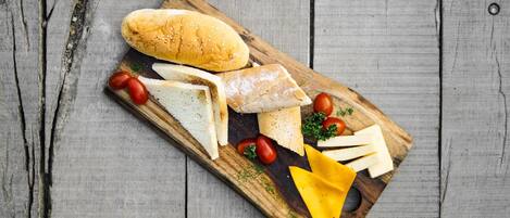A wooden board with various cheeses, tomatoes, and a baguette on a rustic wooden surface.