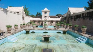 A courtyard with a central fountain, surrounded by potted plants and a building with a tower. - La Luna Resort Yogyakarta (Ngaglik)
