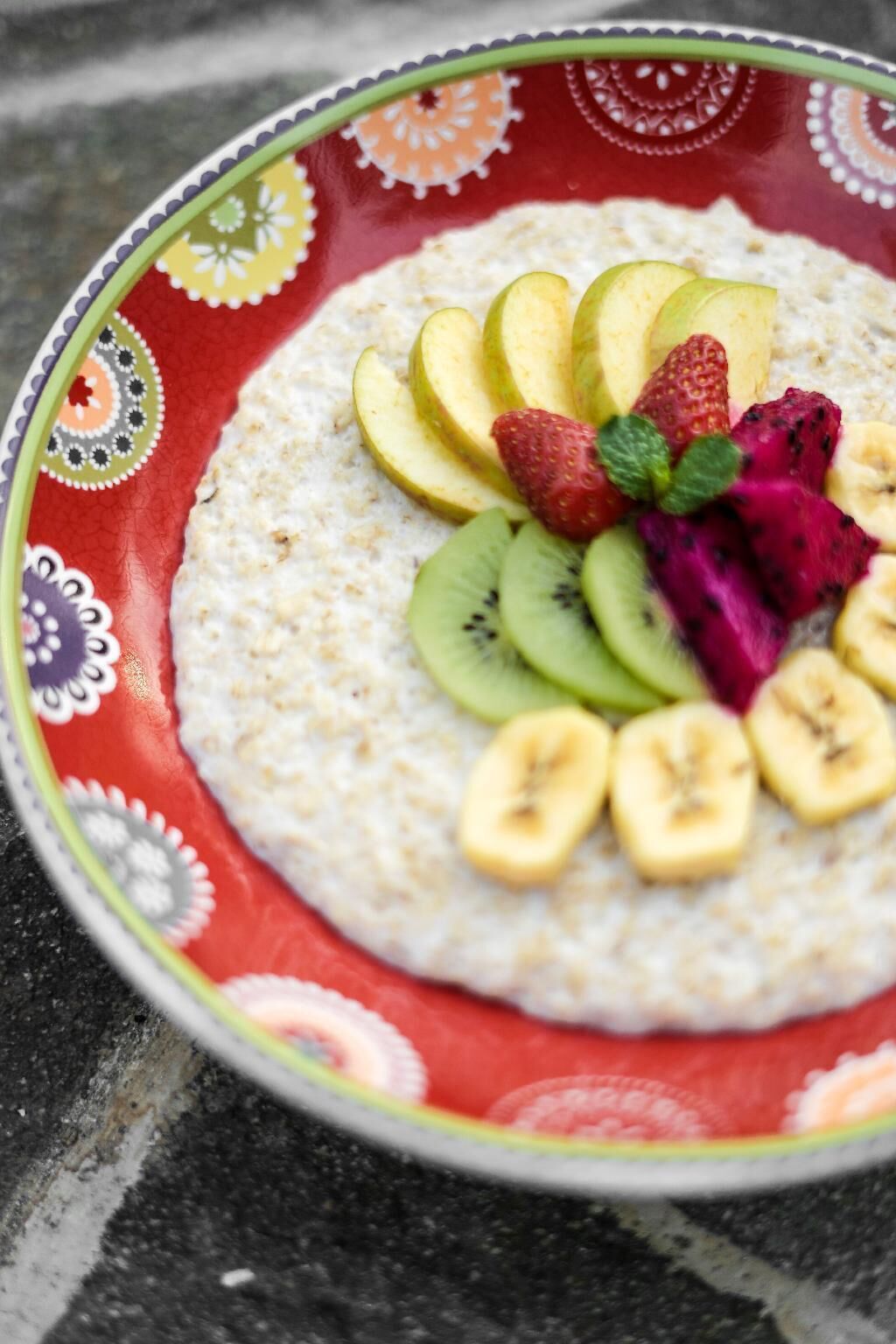 A bowl of oatmeal topped with sliced bananas, strawberries, kiwi, dragon fruit, and a mint leaf.