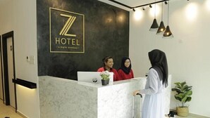 Een hotel receptiebalie met een marmeren aanrecht, een logo erboven en een ontvangstruimte met drie medewerkers.